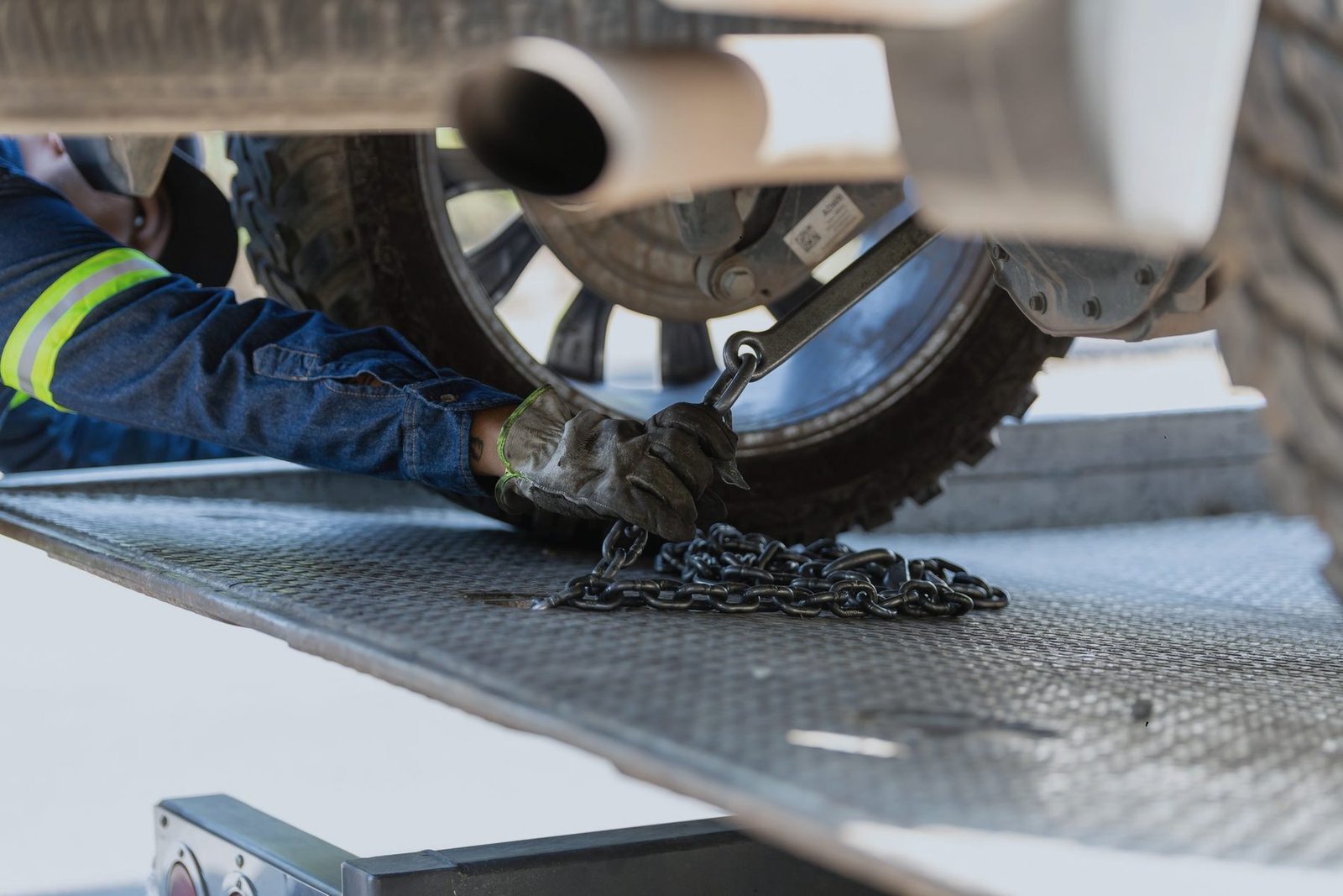 Gloved hands setting a chain around the wheel of a pickup on a steel flatbed deck