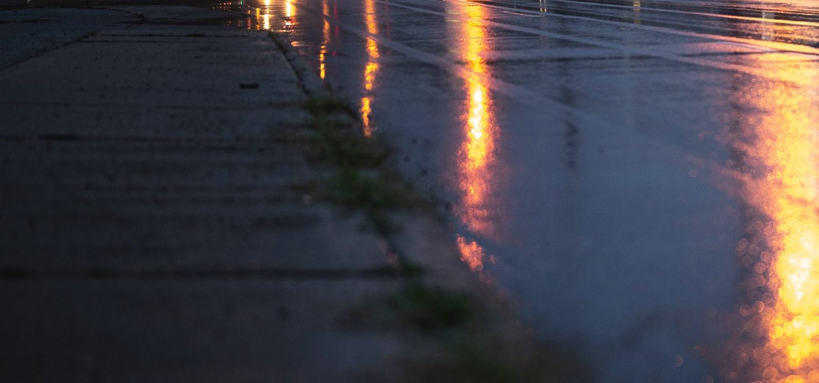 Rain on a city road at night, streetlights reflected in long amber streaks on the asphalt