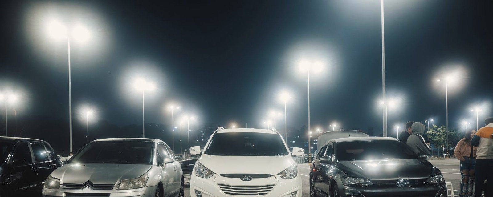 Rows of parked cars under bright lot lights at night