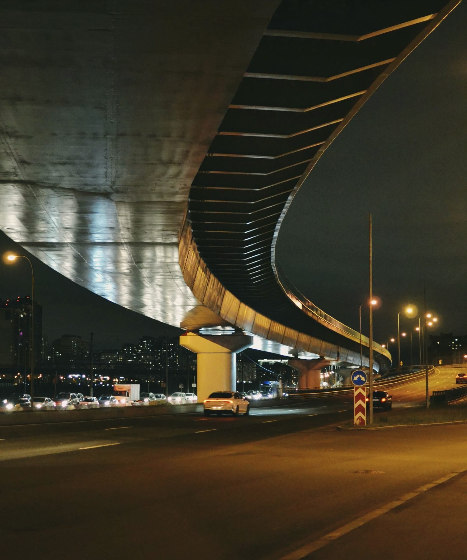 Empty road curving under a concrete overpass at night, lit amber by street lamps
