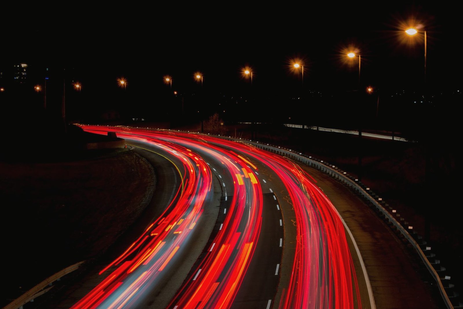 Red tail-light trails sweeping round a highway curve at night