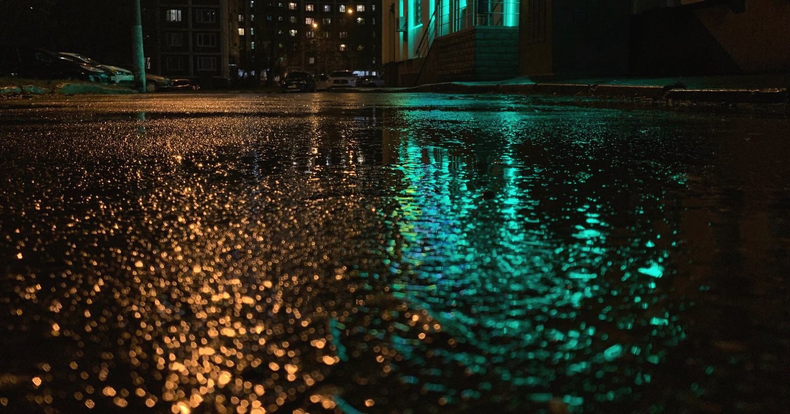 Close view of wet asphalt at night with amber and teal light reflected in it