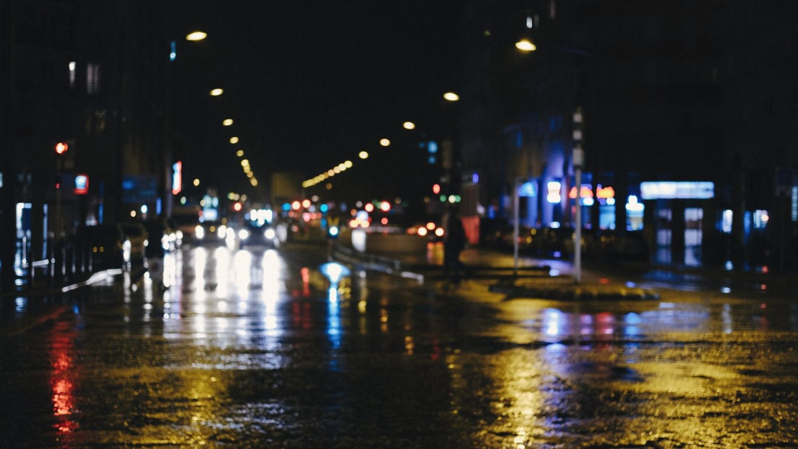 A wet city street at night, streetlights and signals reflected across the junction