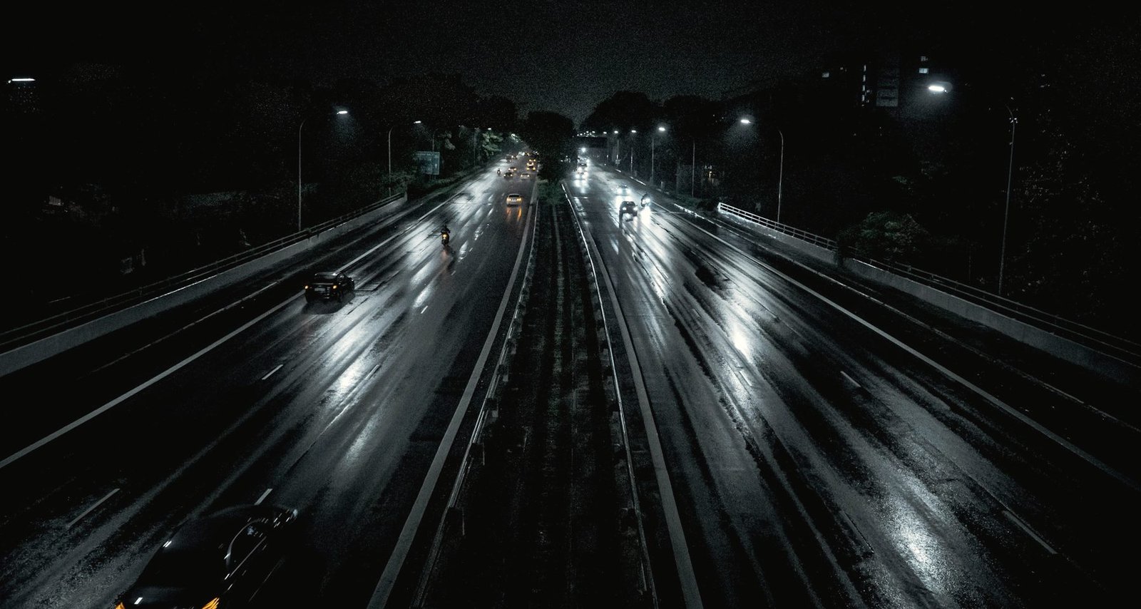 A wet multi-lane highway at night seen from above, lamps reflected in the lanes
